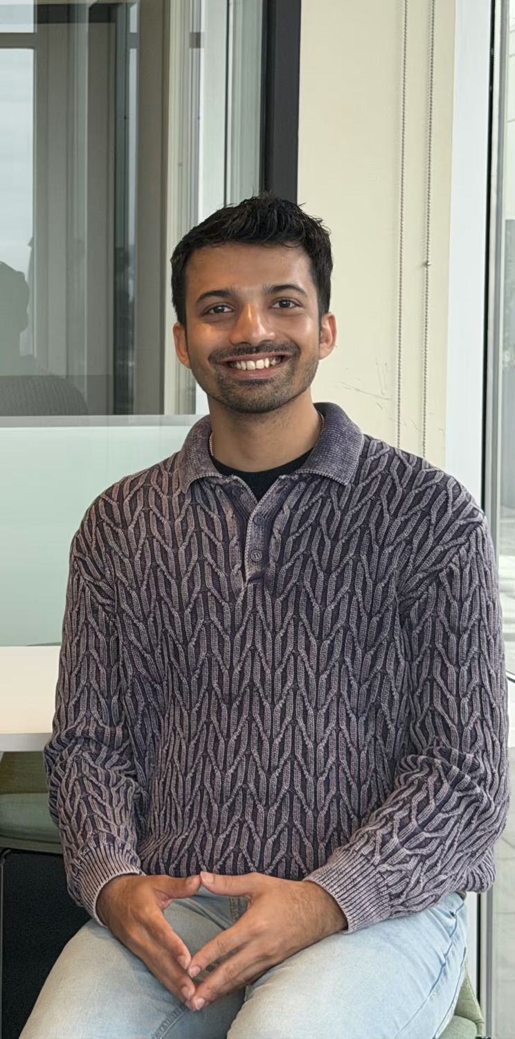 Ashish Dsa seated by an office window in a knit polo, smiling